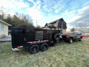 A Trademark Dumpsters trailer parked in front of a damaged house for cleanup and junk removal in Wilmington, DE.