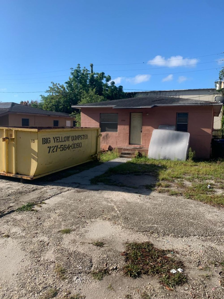A Big Yellow Dumpster placed next to a dilapidated house, suggesting demolition or renovation work by a general contractor in Saint Petersburg, FL.