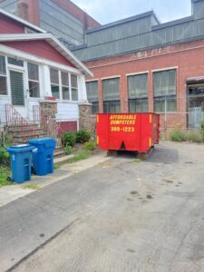 A red dumpster from Affordable Dumpsters placed near a home and industrial building in Watervliet, NY.