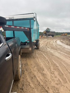 A blue dumpster at a muddy landfill or demolition site with heavy machinery by Site Boss Dumpster Rentals in Raeford, NC.