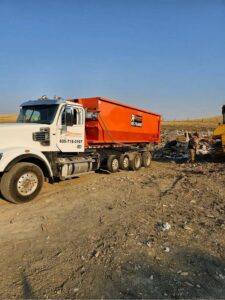 A Rushmore Dumpster truck with an orange roll-off dumpster at a landfill or waste transfer site in Rapid City, SD.