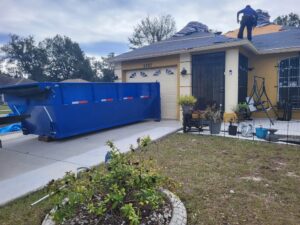A blue dumpster on a driveway at a roofing job site for debris removal by R&Y Dumpster Kings in Tampa, FL.