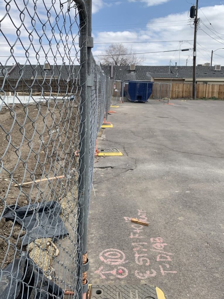 A blue dumpster visible behind a chain-link fence at a construction or cleanup site, used for junk removal by Discount Dumpster in Naples, FL.
