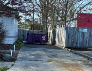 A purple dumpster from JP's Disposal Inc. placed behind a wooden fence in Hampton, VA.