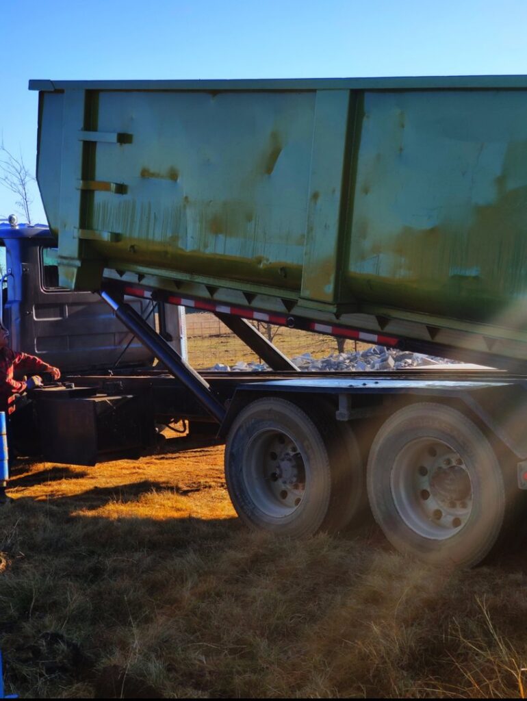 A FJD Waste Disposal and Recycling LLC truck tilting a green dumpster to empty its contents during a junk removal service in Dallas, TX.