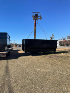 A black dumpster being carefully lifted by heavy equipment for placement by Dumpster Dude in Amory, MS.