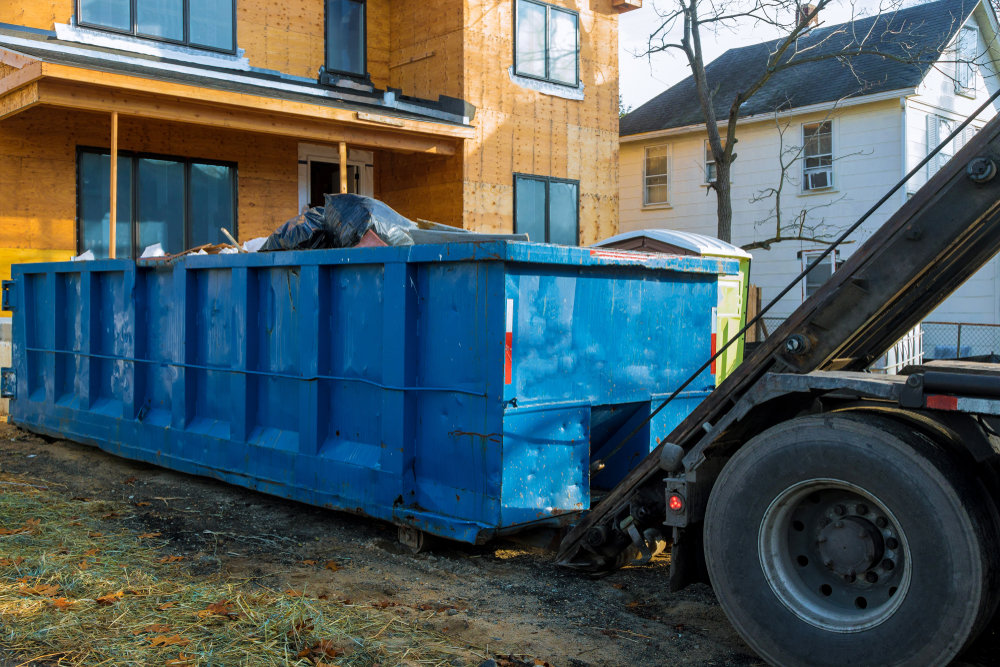 A large blue dumpster filled with debris being loaded onto a truck at a construction site by Dumpster 360 in Clarksville, TN.