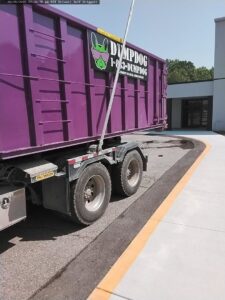 A DumpDog purple dumpster being loaded onto a truck for junk removal services in Flint, MI.