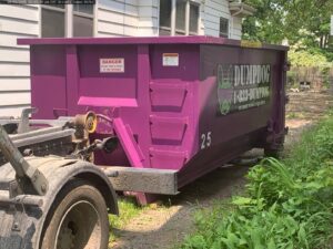 A DumpDog purple dumpster being picked up by a truck after a junk removal job in Flint, MI.