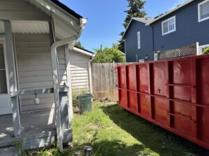 A red dumpster from Cascade Container and Recycling placed between a house and a fence in Seattle, WA.