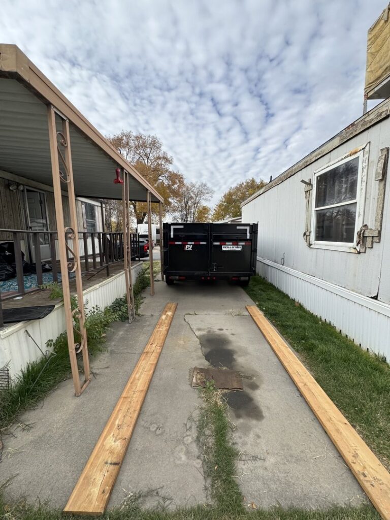 An empty DumpsterDash-LLC dumpster in Ogden, UT, placed between two mobile homes for junk removal.