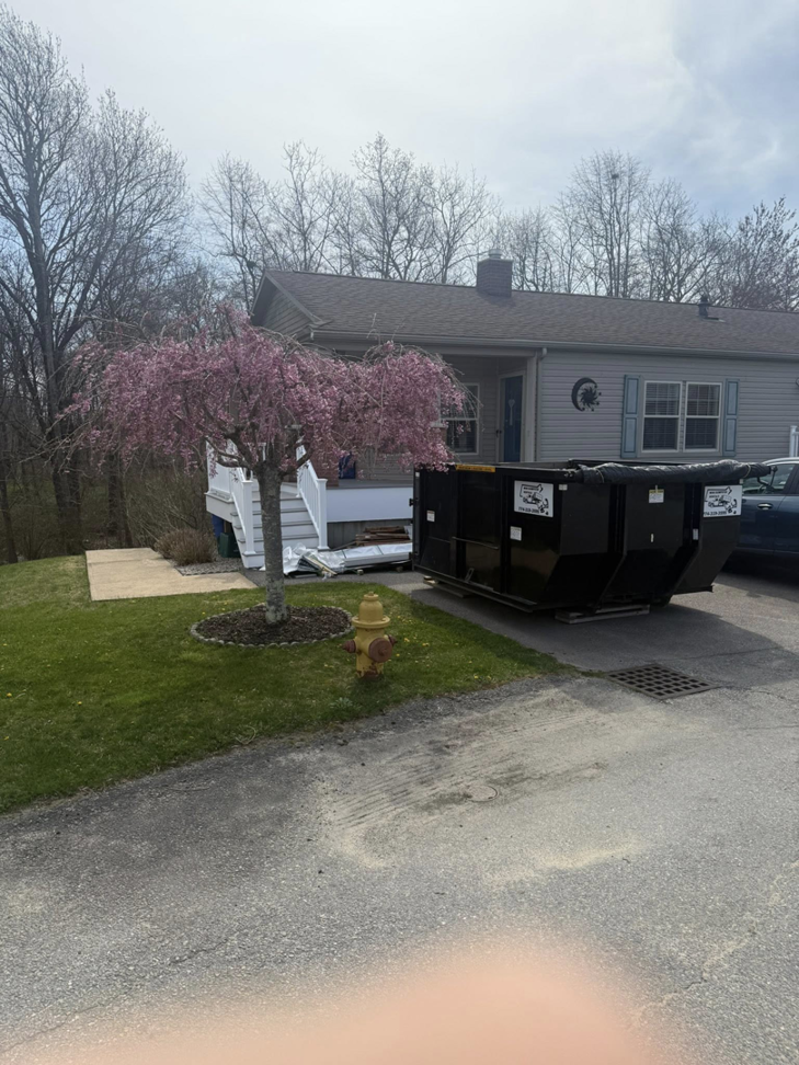 A black dumpster from Mini Dumpster Rentals positioned on a driveway next to a house and a fire hydrant in New Bedford, MA.