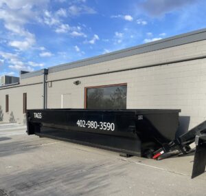A large black Tags Dumpsters roll-off dumpster positioned next to a commercial building in Omaha, NE.