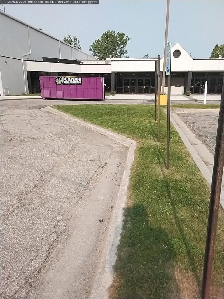 A DumpDog purple dumpster in a commercial parking lot for business junk removal in Flint, MI.