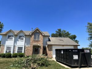A 402 Container dumpster on a residential driveway with construction debris nearby in Omaha, NE.