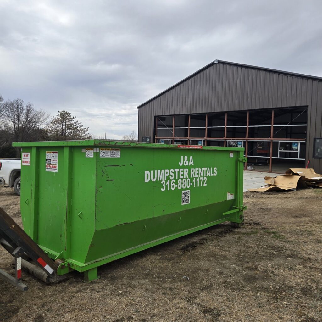 A green J & A Haul Away & Dumpster Rentals dumpster at a construction site in Derby, KS.