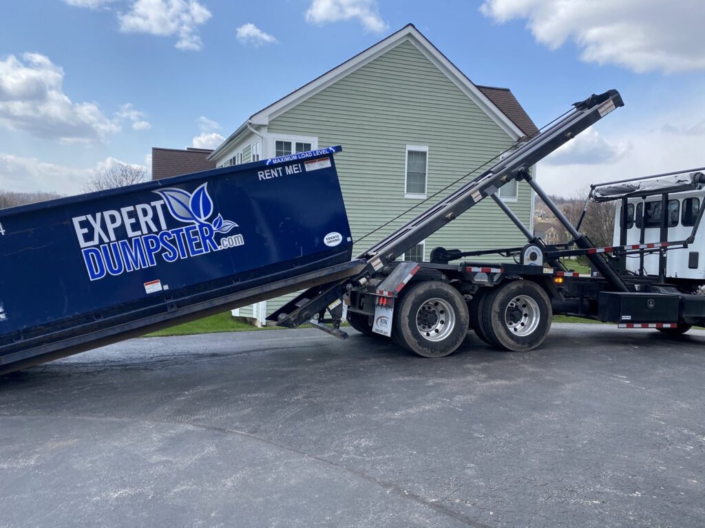 An Expert Dumpster truck delivering a roll-off container to a residential driveway for junk removal in Rochester, NY.