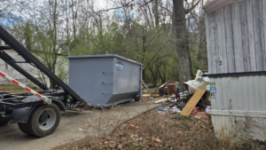 A Creative Disposal Services truck delivering a dumpster for junk removal next to a pile of debris in Macon, GA.