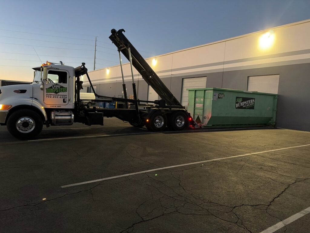 A Junk Control roll-off truck placing or picking up a green dumpster at a commercial building in Henderson, NV.