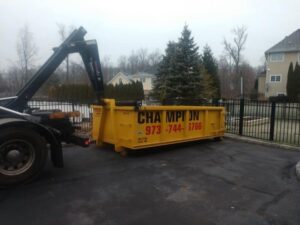 A Champion Waste Removal, Inc. truck delivering or picking up a yellow dumpster at a residential property in Orange, NJ.