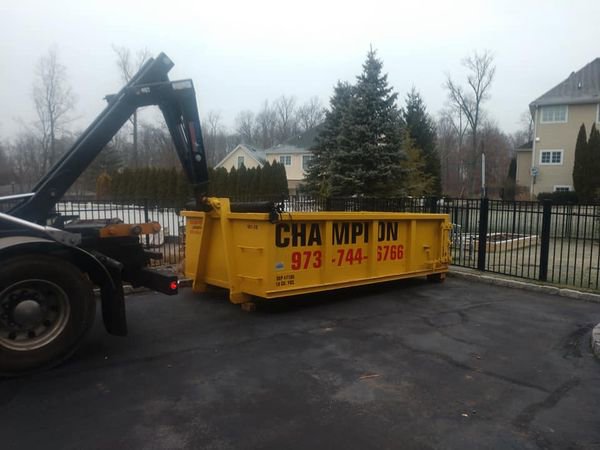 A Champion Waste Removal, Inc. truck delivering or picking up a yellow dumpster at a residential property in Orange, NJ.