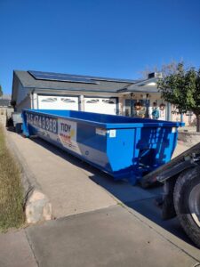A blue Tidy up time dumpster being delivered or picked up by a truck in a residential driveway in El Paso, TX.