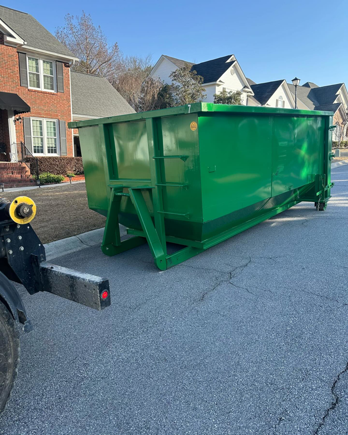A green dumpster from Dumpster on Demand being delivered or picked up by a truck on a street in Columbia, SC.