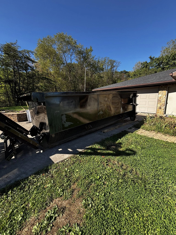 A black roll-off dumpster being delivered or picked up by Wagners Property Services LLC in front of a residential home in Canton, OH.