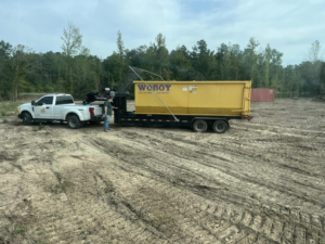 A WoBoy LLC truck delivering a large yellow dumpster for junk removal services in West Monroe, LA.