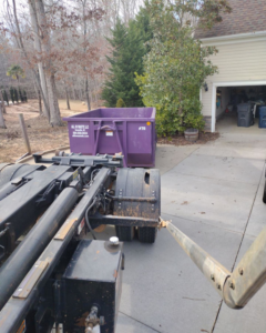 A purple All In Waste dumpster being delivered to a residential driveway in Greenville, SC.