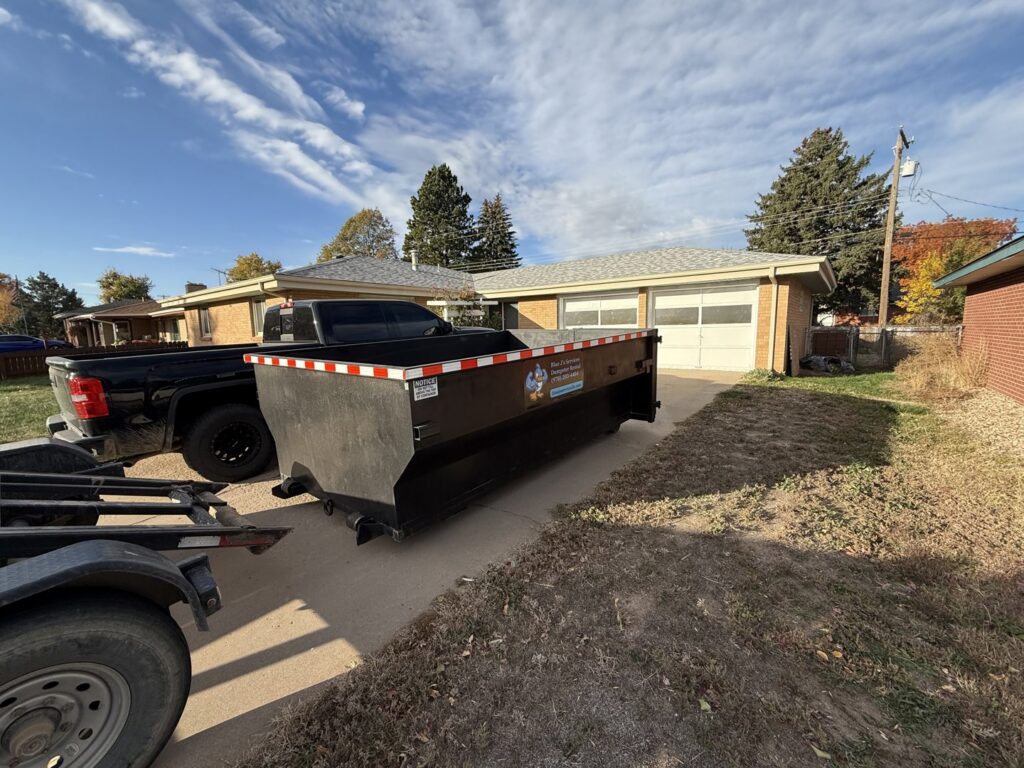 A Blue J's Services Dumpster Rental truck delivering an empty dumpster to a residential driveway in Greeley, CO.