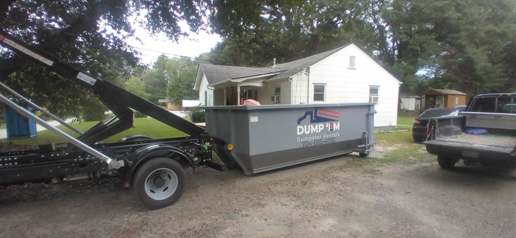 A Dump 'Em Dumpster Rentals truck delivering a dumpster to a residential property in Charlotte, NC.