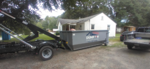 A Dump 'Em Dumpster Rentals truck delivering a dumpster to a residential property in Charlotte, NC.