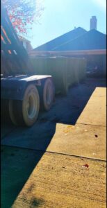 A FJD Waste Disposal and Recycling LLC truck delivering a green dumpster to a residential property for junk removal in Dallas, TX.