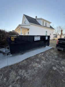 An H & H Dumpster Rental truck delivering an empty dumpster to a residential property in Rootstown, OH.