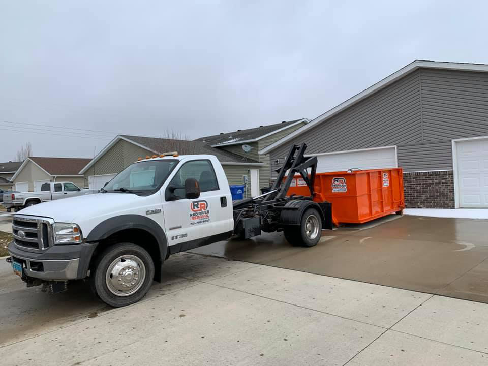 A Red River Removal truck delivering a roll-off dumpster to a residential driveway in West Fargo, ND.