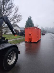 An orange roll-off dumpster being delivered or picked up on a residential street by ADE Hauling in Tacoma, WA