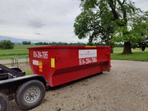 A red dumpster being delivered to a rural property by Trinity Dumpster Rental LLC in Kansas City, MO.