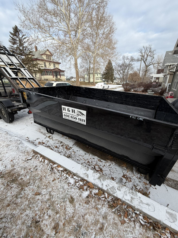 An H & H Dumpster Rental truck delivering an empty dumpster on a snowy residential street in Rootstown, OH.