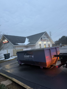 A Dump 'Em Dumpster Rentals truck delivering a dumpster in front of a TitleMax building in Charlotte, NC.