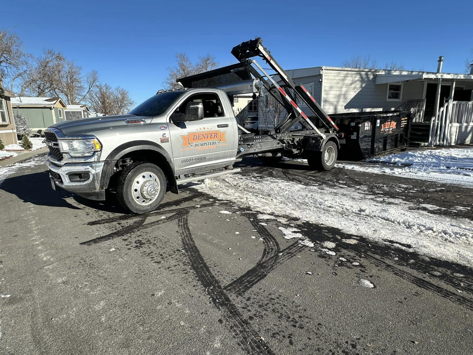 A Denver Dumpsters truck delivering or picking up a roll-off dumpster at a residential property in Denver, CO.