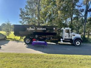A Parish Dumpsters, LLC truck delivering a large black dumpster on a residential driveway in Baton Rouge, LA.