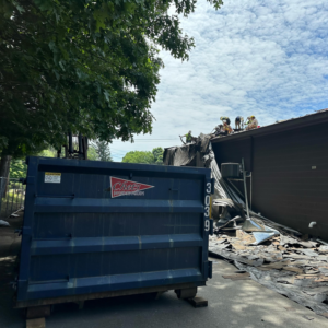 A Chet's Disposal dumpster at a demolition site with debris and workers on the roof in Springfield, MA.