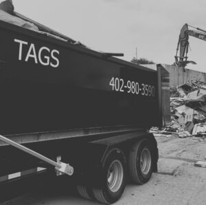 A Tags Dumpsters roll-off dumpster at a demolition site with an excavator and debris in the background in Omaha, NE.