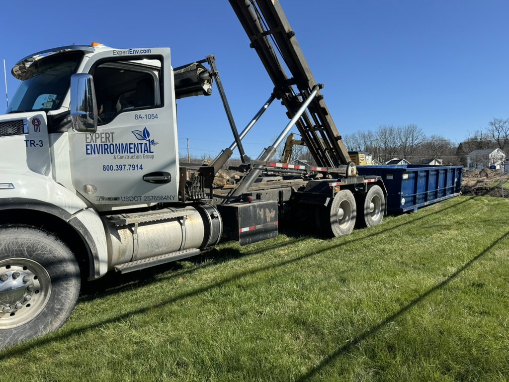 An Expert Dumpster truck deploying a roll-off container for a junk removal project in Rochester, NY.