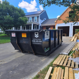 A large black roll-off container from Dumpster Dogs placed on a driveway at a construction site in Somerset, MA.