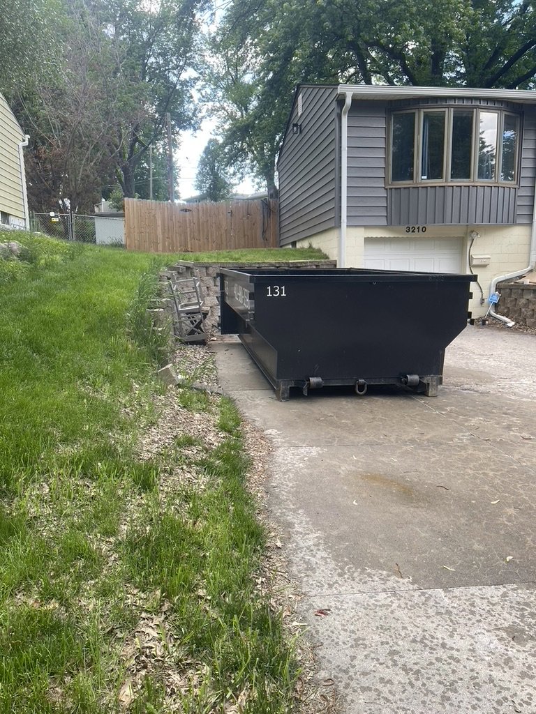 A black Tags Dumpsters roll-off dumpster positioned in a residential driveway for junk removal in Omaha, NE.