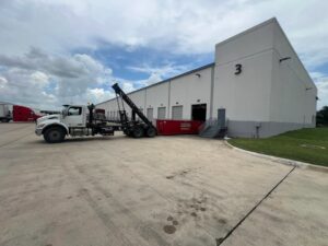 A redbox+ truck dropping off a dumpster at a commercial building for redbox+ Dumpsters of Greater Austin in Austin, TX