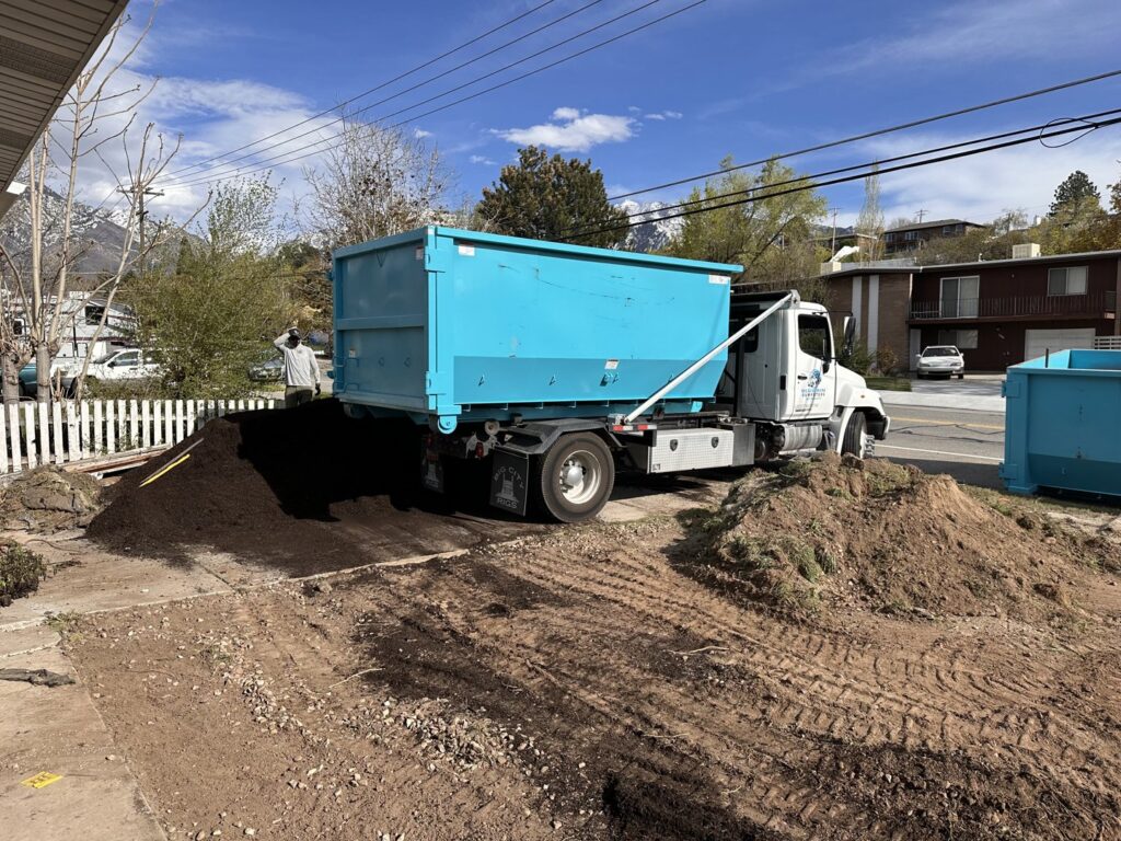 A Blue Bin Dumpster Rentals truck dropping off a dumpster for a landscaping project in Millcreek, UT.