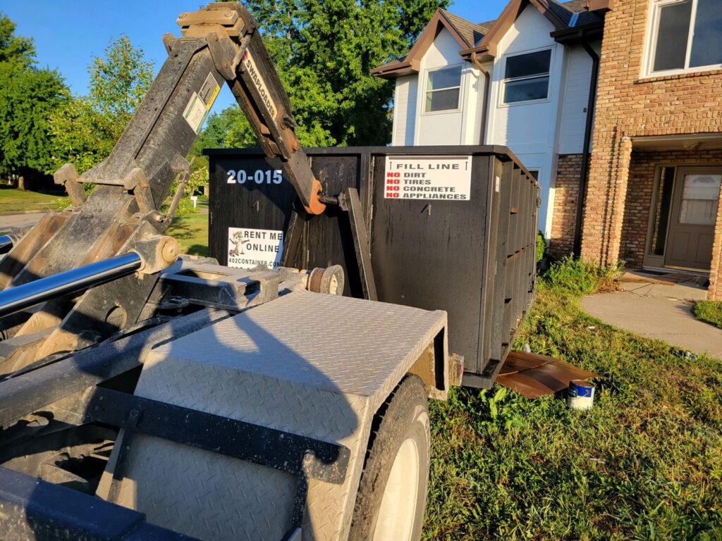 A 402 Container truck dropping off a dumpster at a residential property for junk removal in Omaha, NE.
